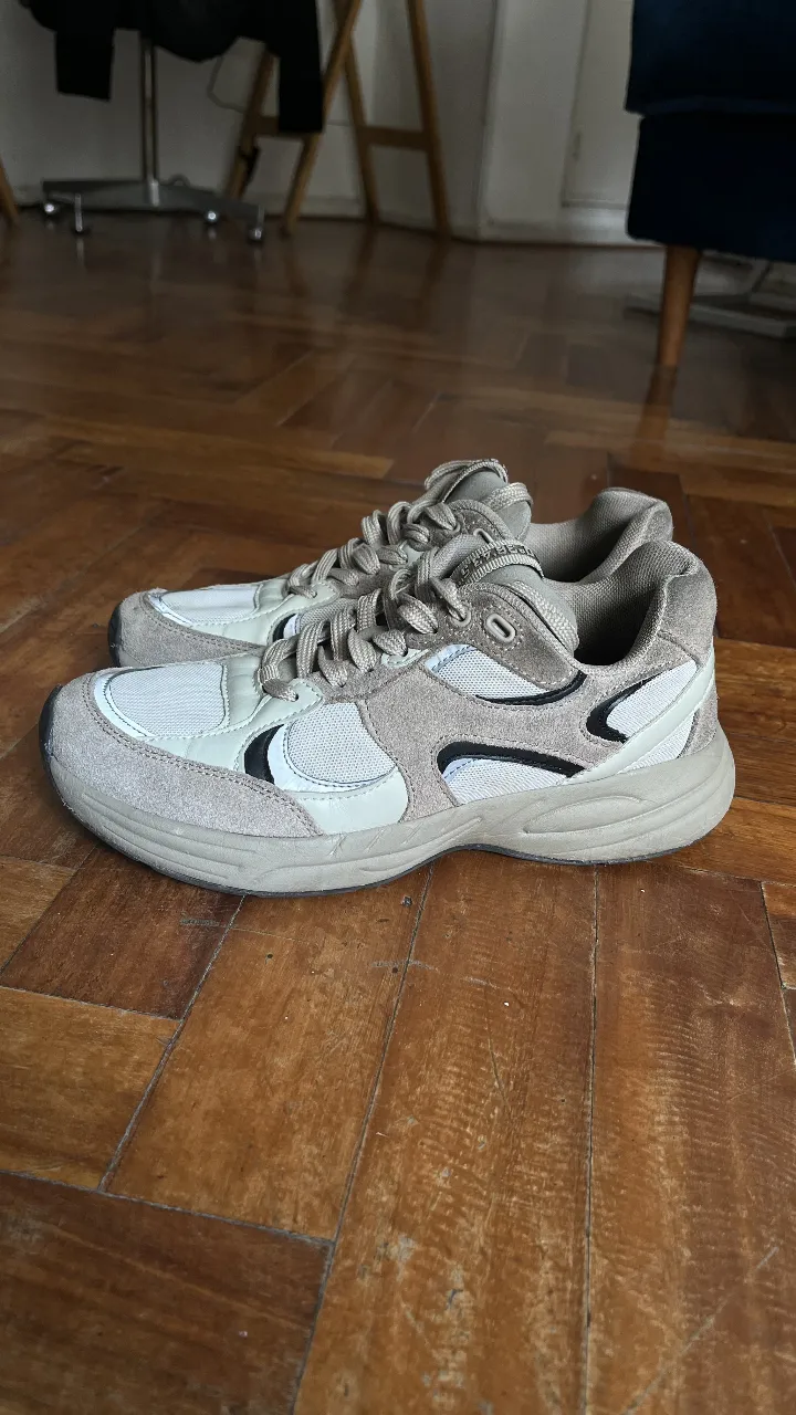 Zapatillas deportivas para mujer en tonos neutros. Diseño moderno con detalles en negro y beige. Ideales para un look casual y cómodo.