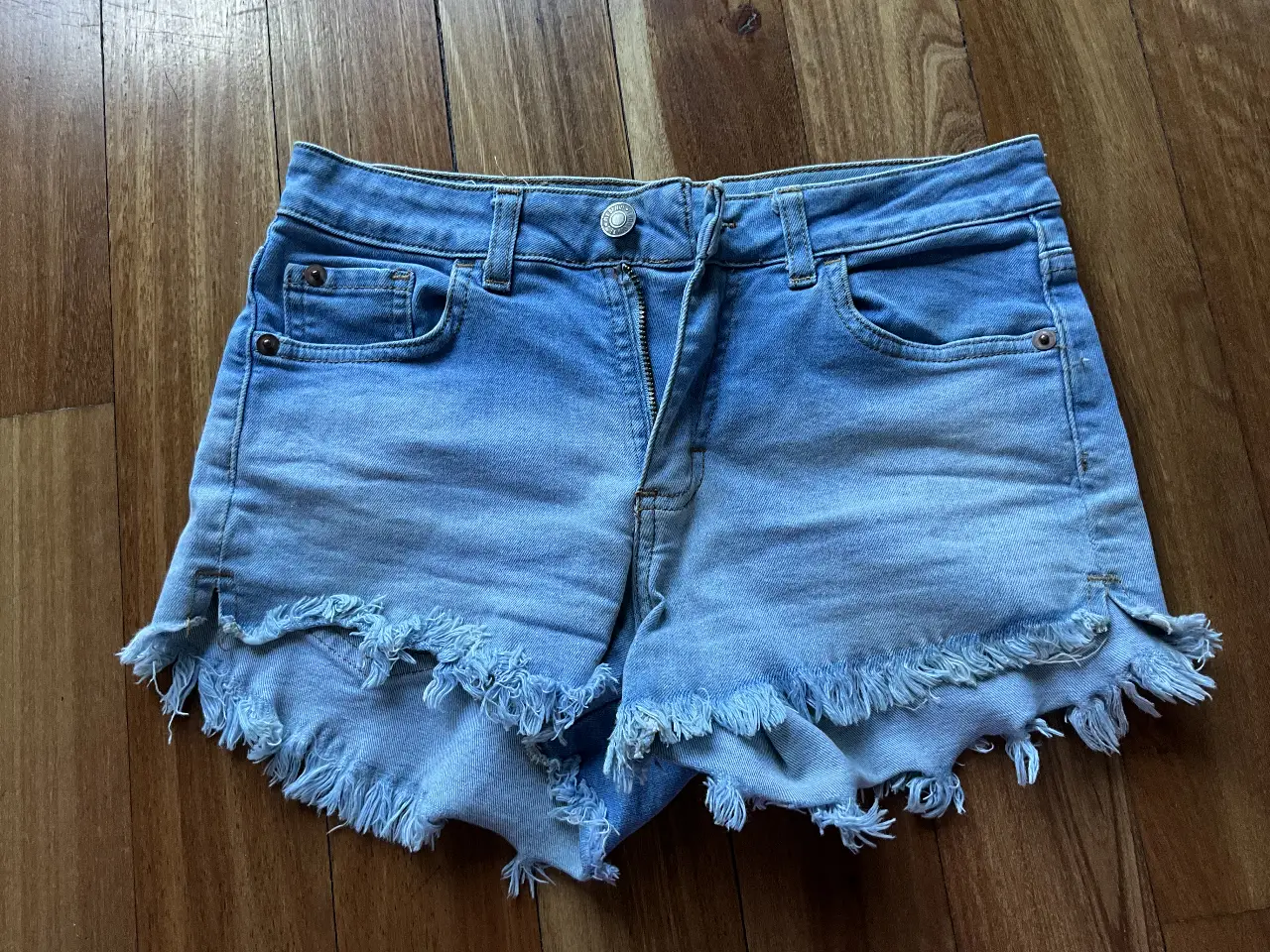 Short de jean de mujer, tiro medio, con detalles desflecados en el borde inferior. Ideal para un look casual y fresco.