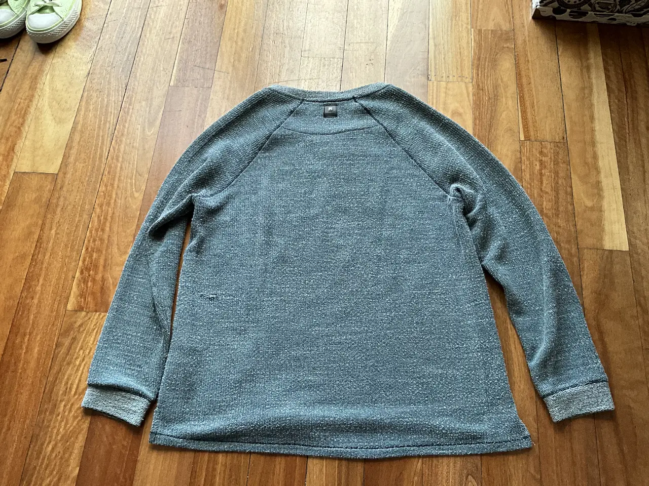 Buzo de cuello redondo gris con mangas largas. Diseño liso con detalle de etiqueta en el cuello. Ideal para un look casual y cómodo.