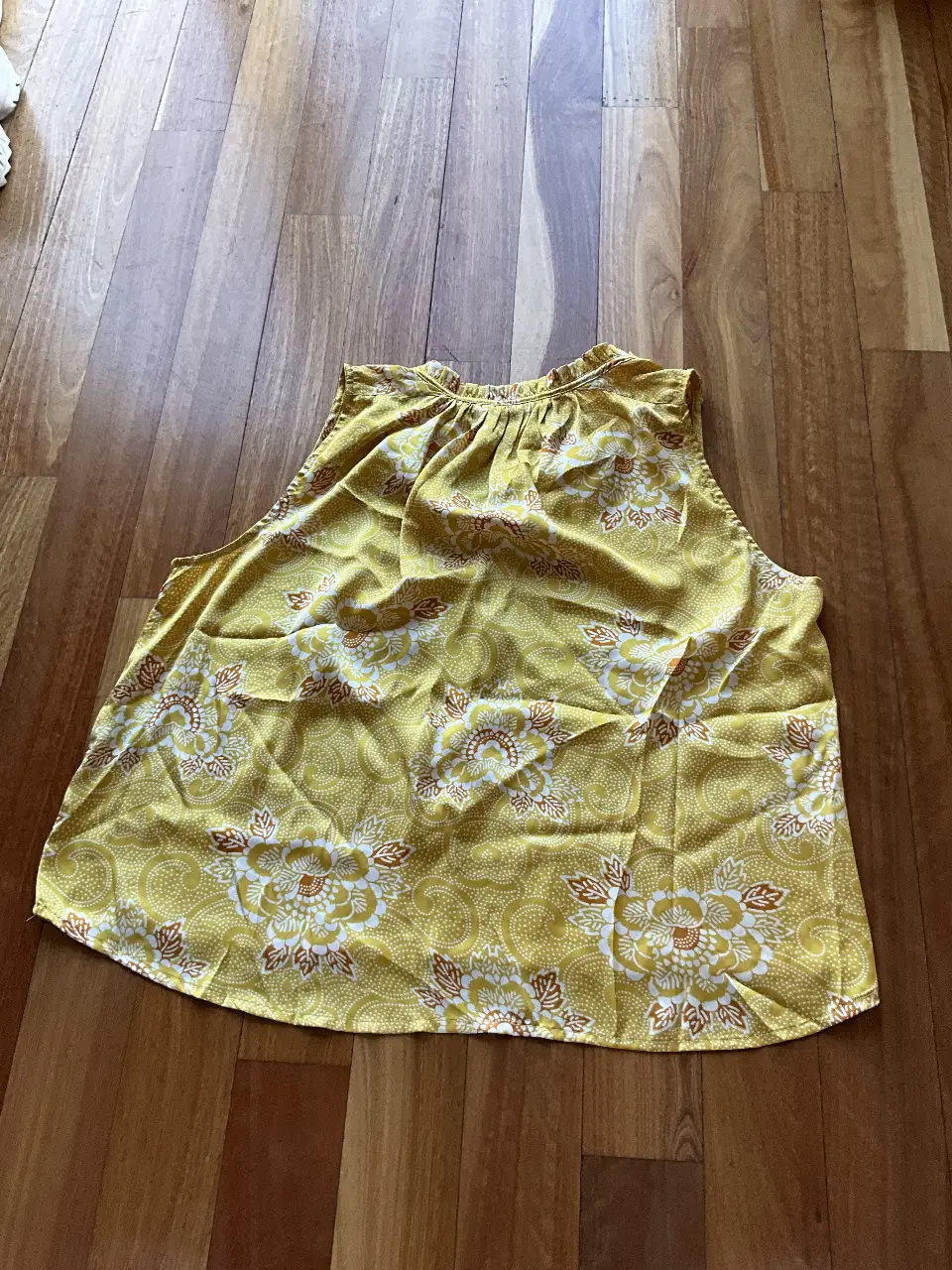 Blusa sin mangas de color amarillo con estampado floral en blanco y marrón. Cuello redondo con detalle fruncido y lazo. Ideal para un look fresco y primaveral.