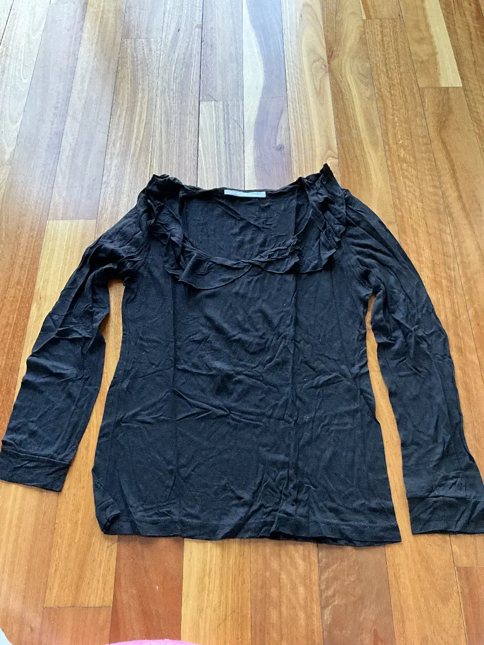 Blusa negra de manga larga con detalle de volados en el cuello. Ideal para un look elegante y sofisticado.