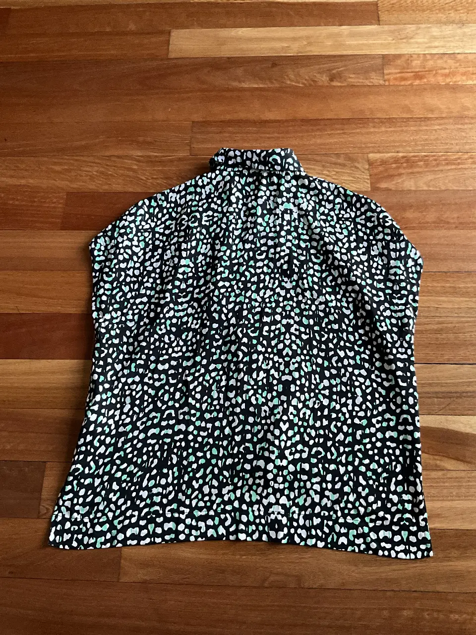 Blusa estampada con diseño de lunares en blanco y negro, con detalles en verde. Cuello alto y manga corta. Ideal para un look elegante y moderno.