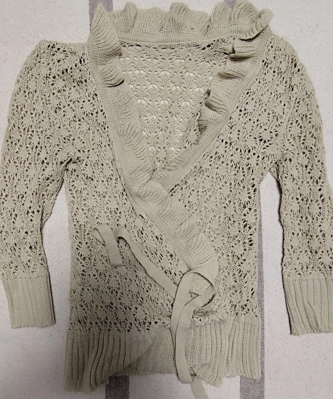 Cardigan tejido de punto calado con detalle de volados en el cuello y cierre con lazos. Ideal para un look casual y femenino.