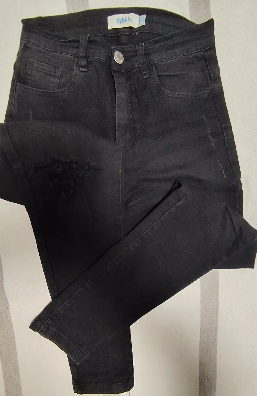 Jeans negro con roturas en la rodilla, tiro medio y corte skinny. Ideal para un look casual y moderno.