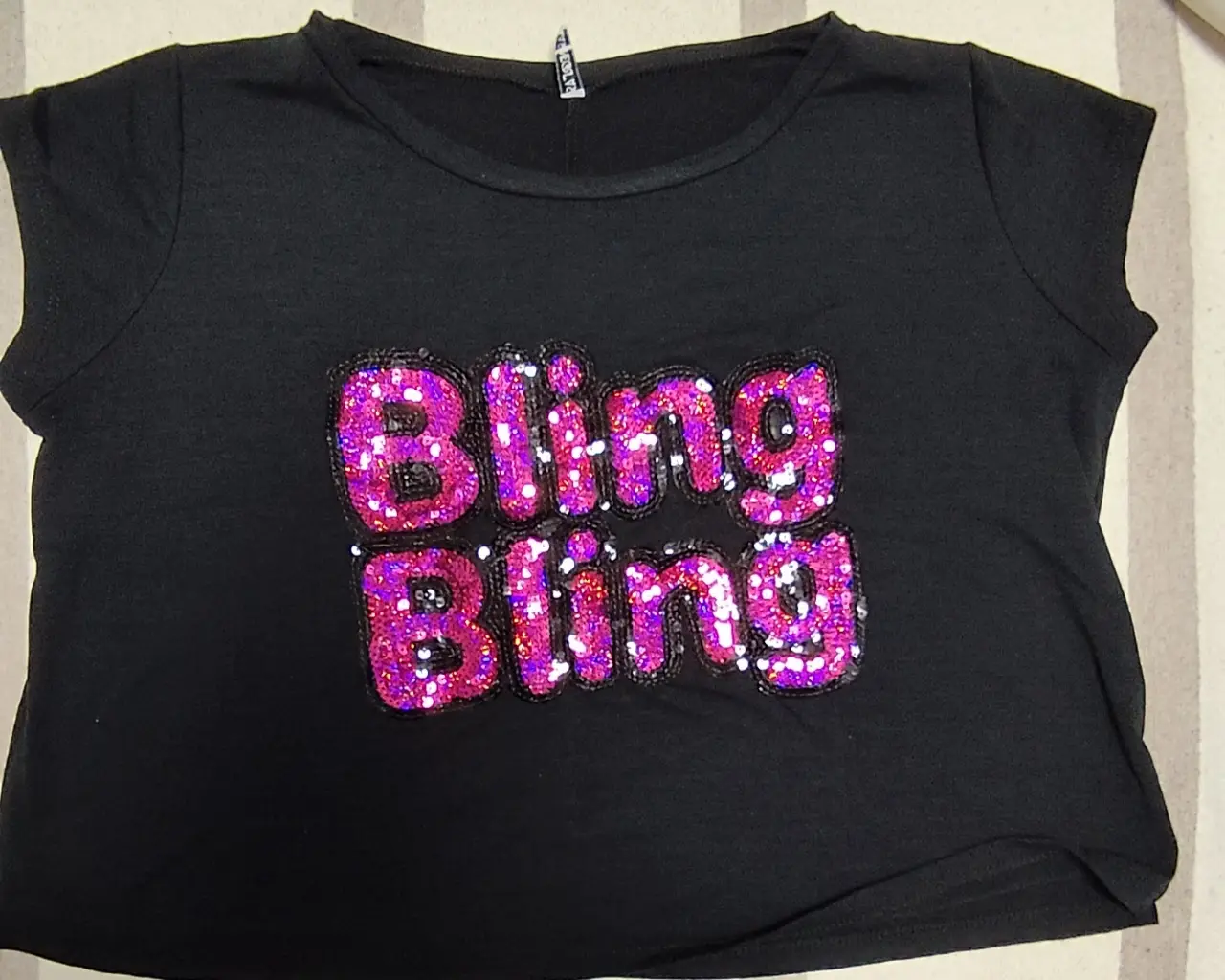 Remera negra de manga corta con aplique "Bling Bling" en lentejuelas rosas y negras. Ideal para un look casual y con onda.