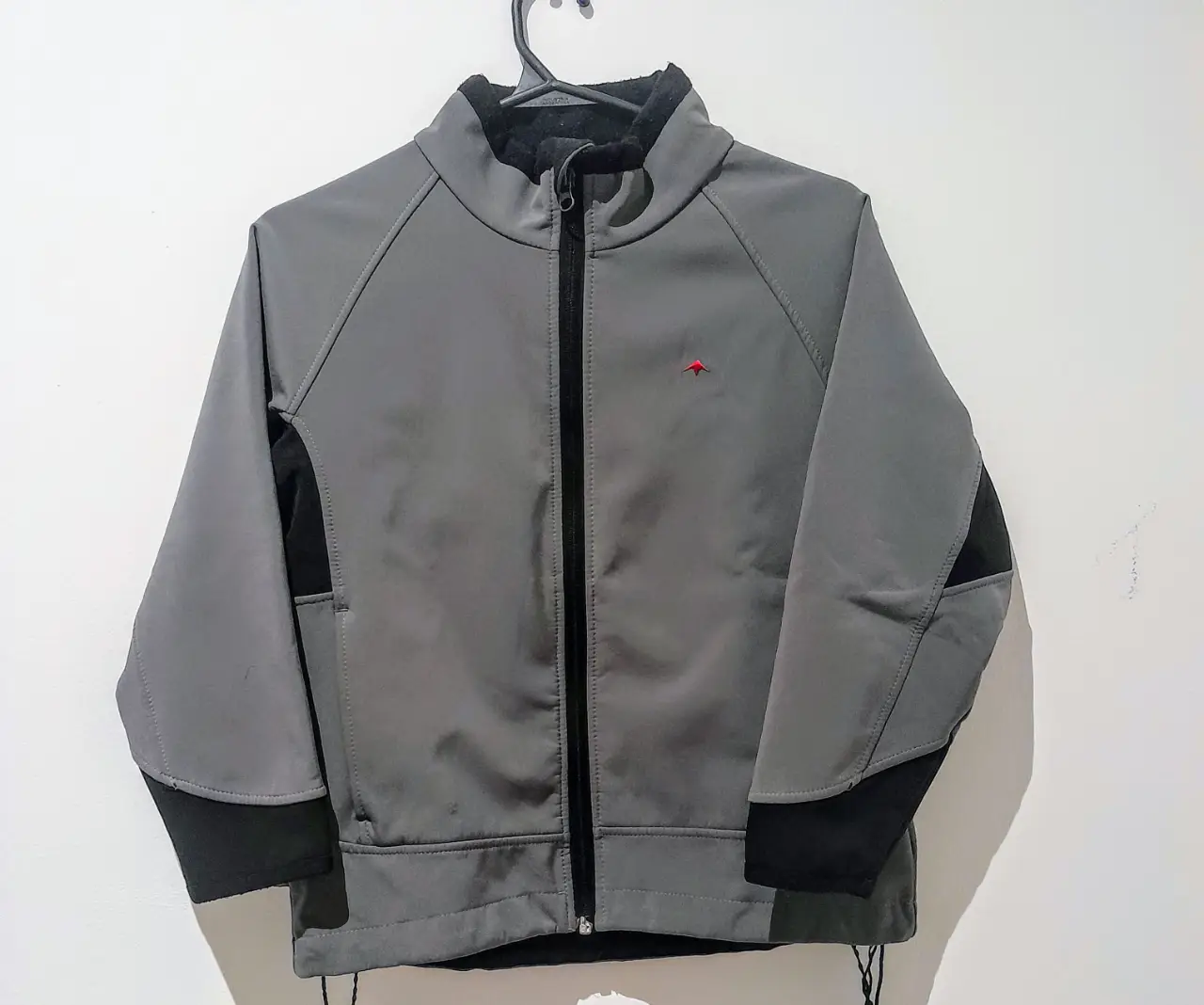 Campera Montagne gris con detalles en negro, Alta montaña y Sky. Posee cierre frontal, cuello alto y un pequeño logo rojo. Confeccionada con tecnología Shark Skin.  Impermeable, resistente y diseño funcional.