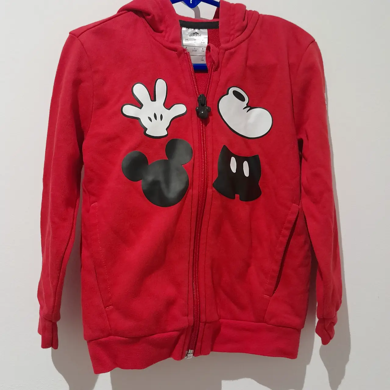 Buzo con cierre rojo para niño con diseño de Mickey Mouse. Cuenta con capucha y detalles en blanco y negro. Ideal para un look casual y cómodo.