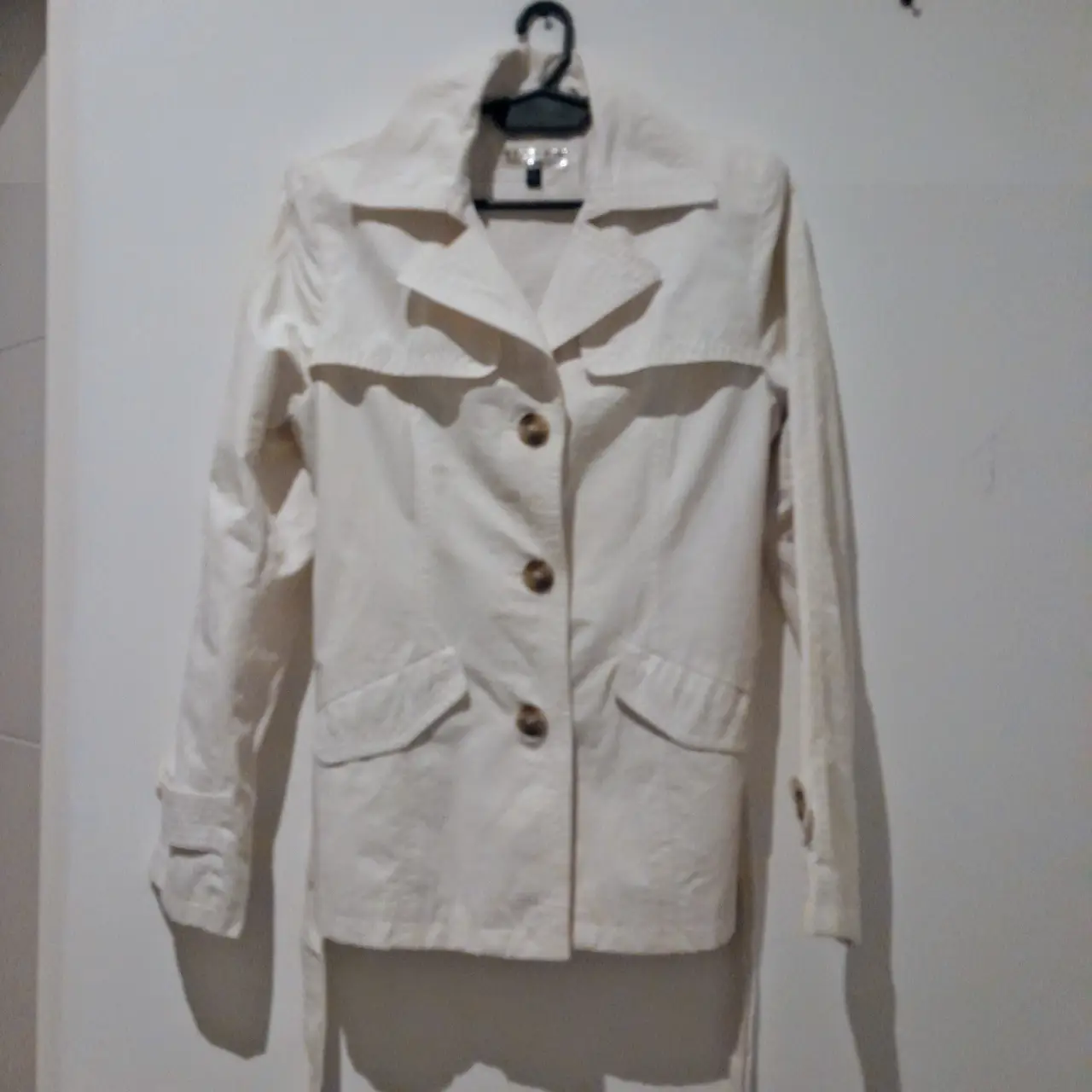 Elegante trench coat impermeable corto color crudo, ideal para un look sofisticado. Confeccionado con tela de calidad, este trench presenta un diseño clásico con botones y cinturón para ajustar la cintura. Perfecto para complementar cualquier outfit.