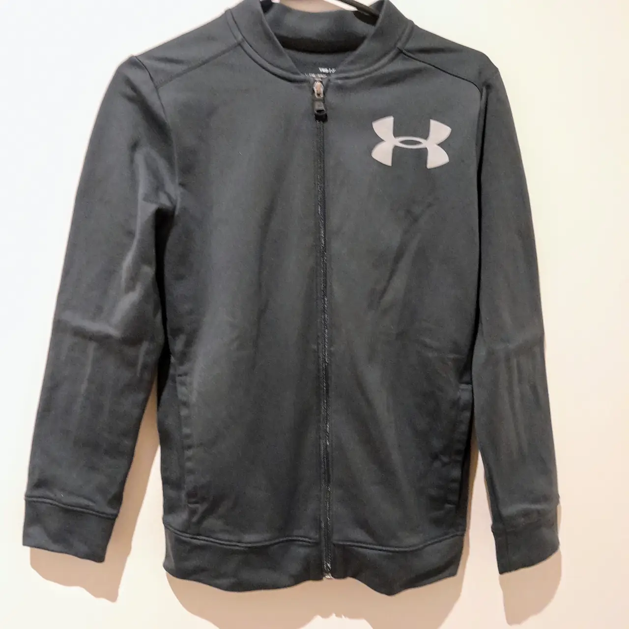 Buzo deportivo con cierre de la marca Under Armour. Color gris oscuro, ideal para actividades deportivas o uso casual.