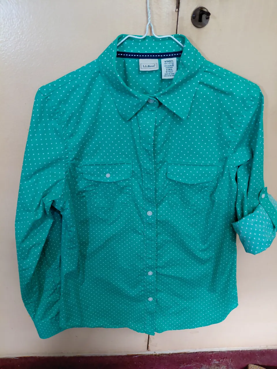 Camisa manga larga verde con lunares blancos. Tiene dos bolsillos en el frente y se puede enrollar las mangas.