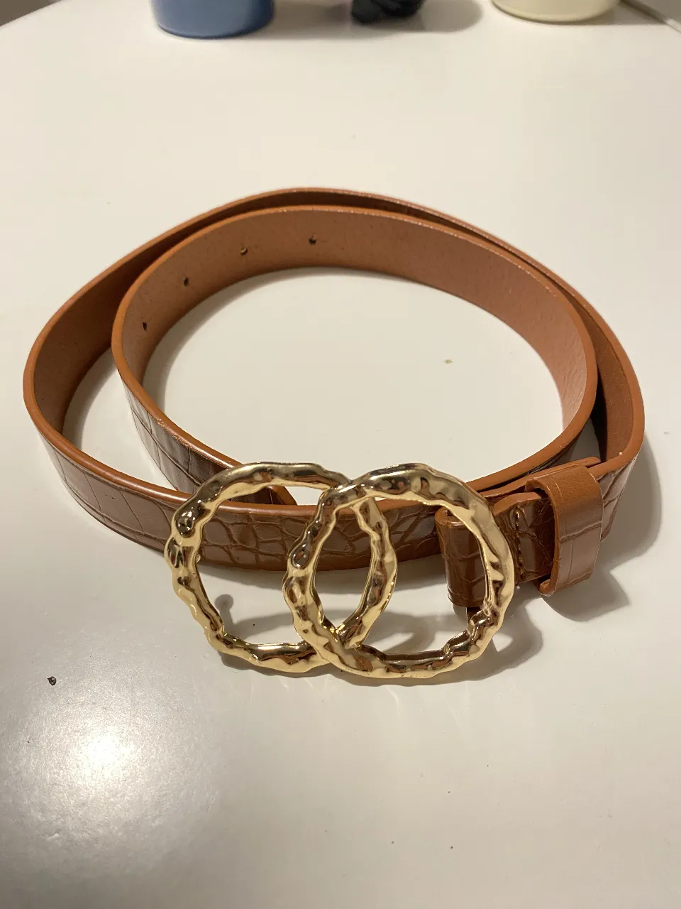 Cinturón marrón con hebilla doble dorada y textura de cocodrilo. Ideal para darle un toque chic a cualquier outfit.