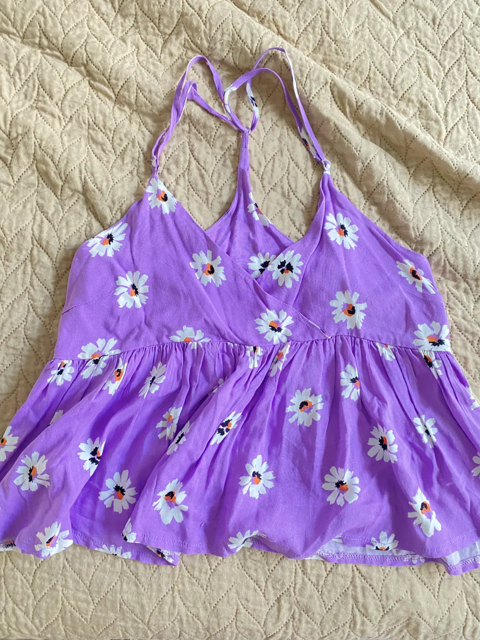 Top violeta con estampa de flores blancas y detalles en naranja. Breteles finos y escote cruzado. Ideal para un look fresco y femenino.