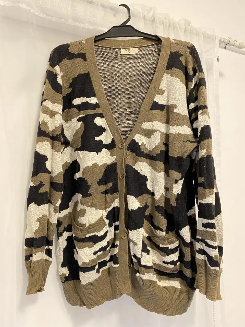 Cardigan de mujer con estampado camuflado en tonos verdes, negro y blanco. Posee dos bolsillos delanteros y cierre con botones. Ideal para un look casual y abrigado.