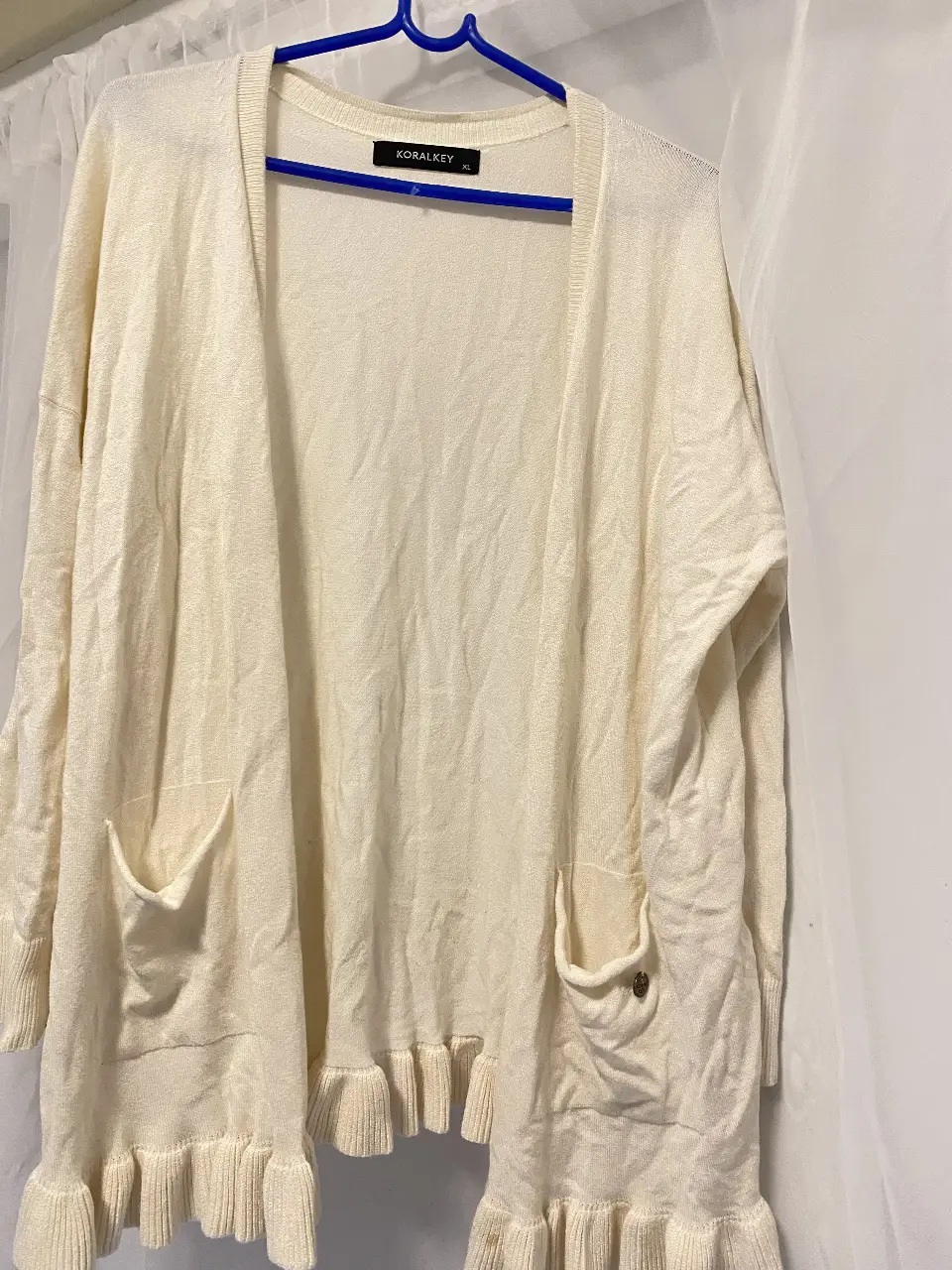Cardigan de tejido liviano color crudo, con dos bolsillos delanteros y detalle de volados en el borde inferior. Ideal para un look casual y cómodo. nuevo