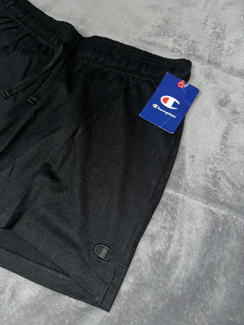 Short deportivo Champion negro para hombre. Confeccionado en tela suave y cómoda, ideal para actividades físicas o uso casual. Cuenta con cintura elastizada con cordón ajustable y el logo de la marca bordado.