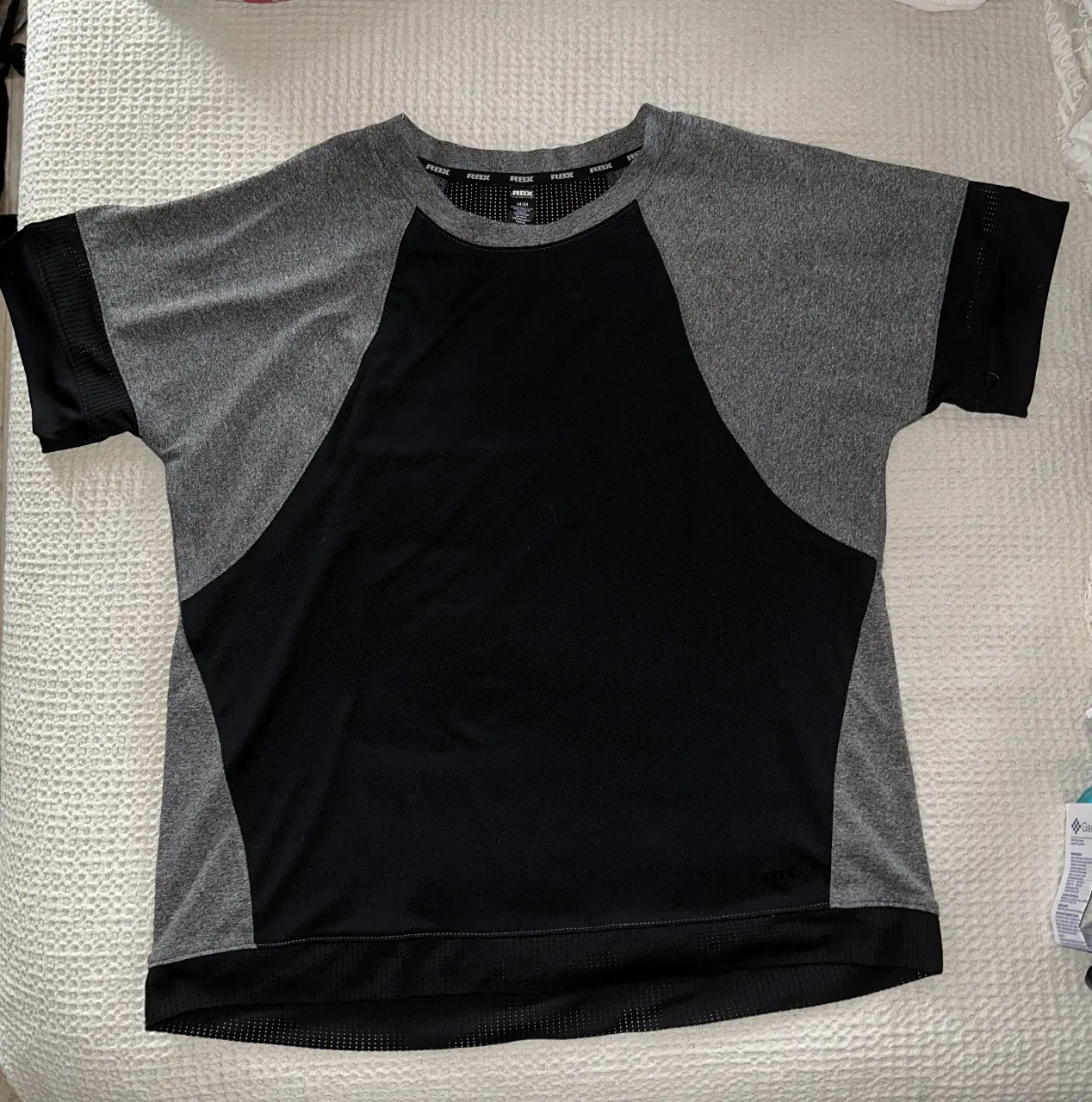 Remera deportiva RBX para mujer, manga corta con paneles en contraste gris y negro. Ideal para entrenamientos y actividades físicas.