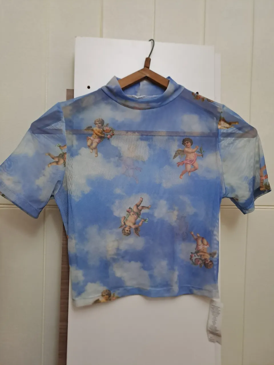Remera manga corta con cuello alto y estampa de nubes y querubines. La tela es translúcida.