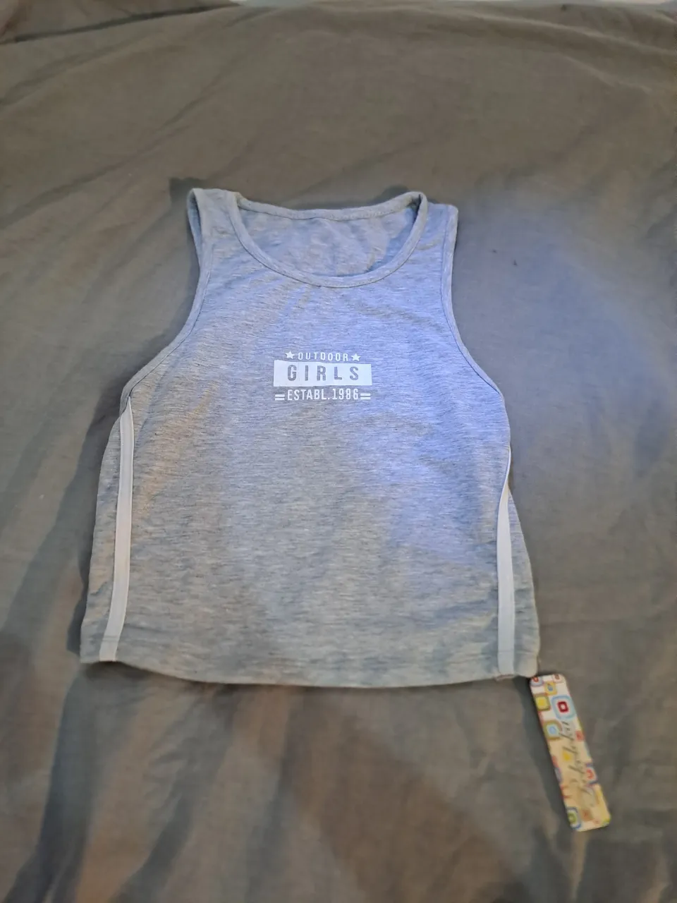 Musculosa gris con estampa "OUTDOOR GIRLS ESTABL. 1986" en el frente. Posee detalles de tiras blancas a los costados y en los hombros.