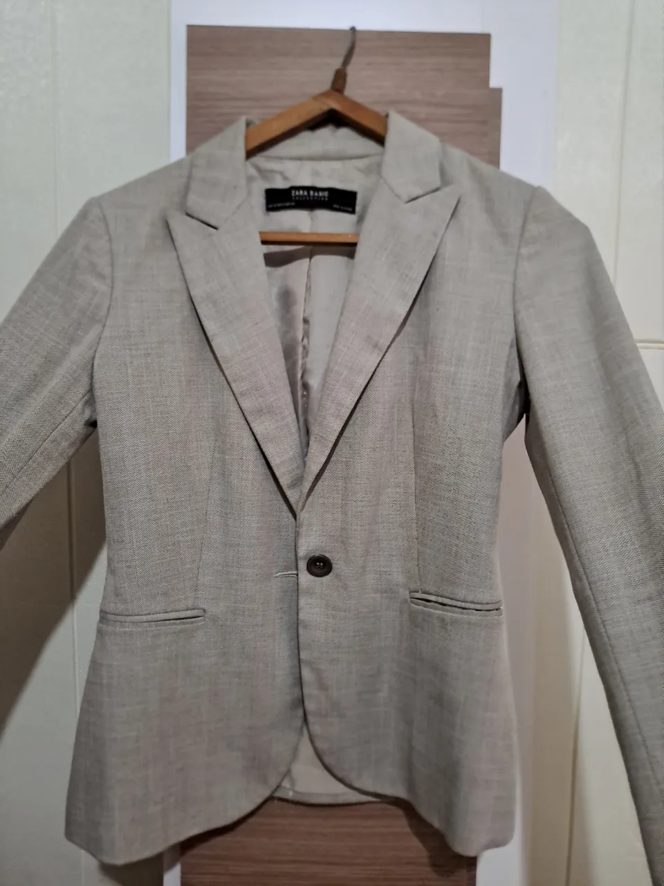 Blazer de color crudo, con un solo botón al frente y bolsillos con solapa. Posee cuello solapa y mangas largas.