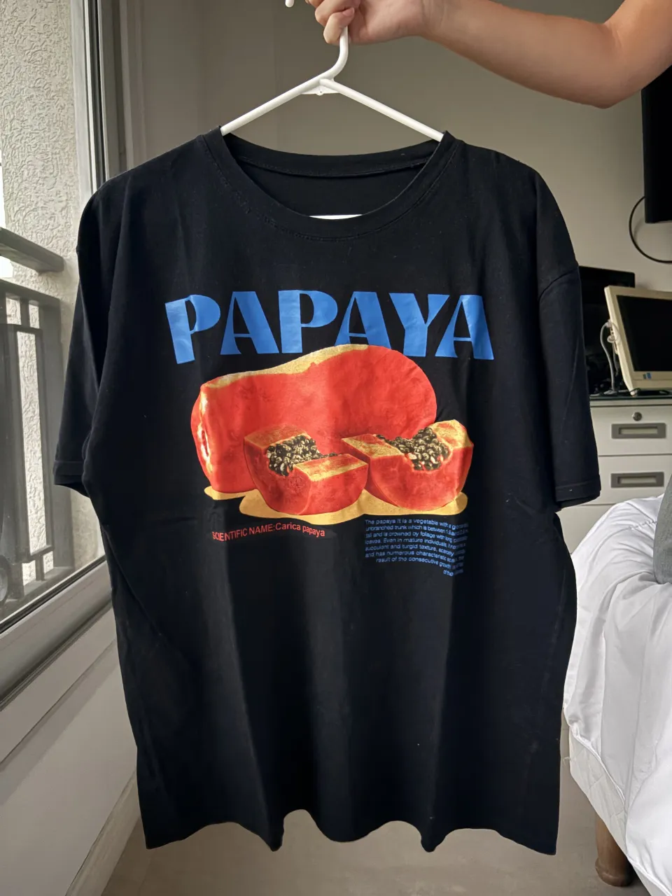Remera negra con estampa de papaya y el texto "PAPAYA" en letras azules. Debajo de la fruta, se lee "SCIENTIFIC NAME: Carica papaya" y una breve descripción botánica.