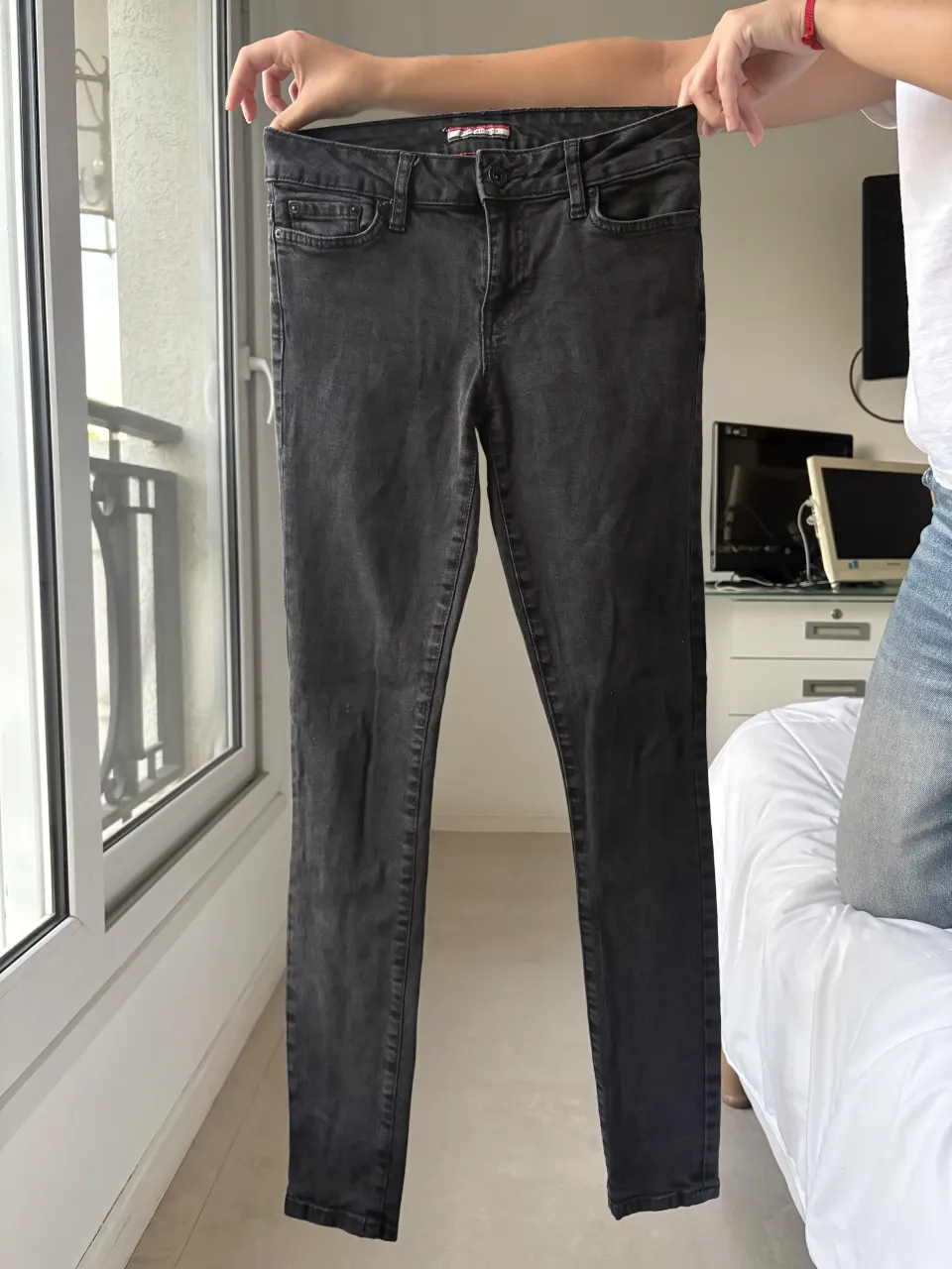 Jeans negros con costuras rojas visibles en la cintura. Poseen bolsillos delanteros y traseros.