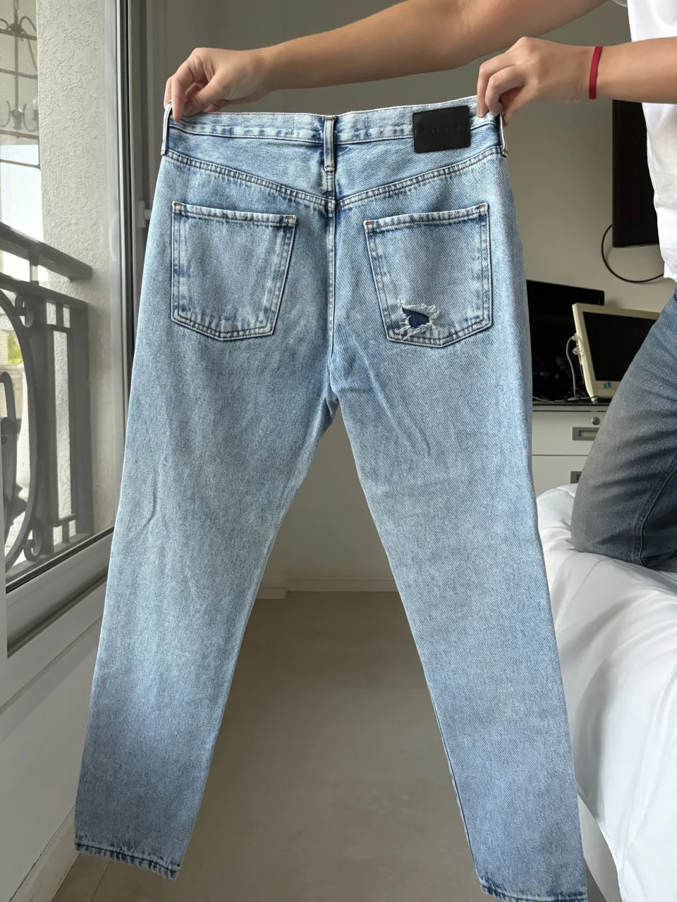 Jeans de algodón celeste con roturas y desgaste. Posee bolsillos delanteros y traseros. La etiqueta de la marca es negra y se encuentra en la parte trasera.