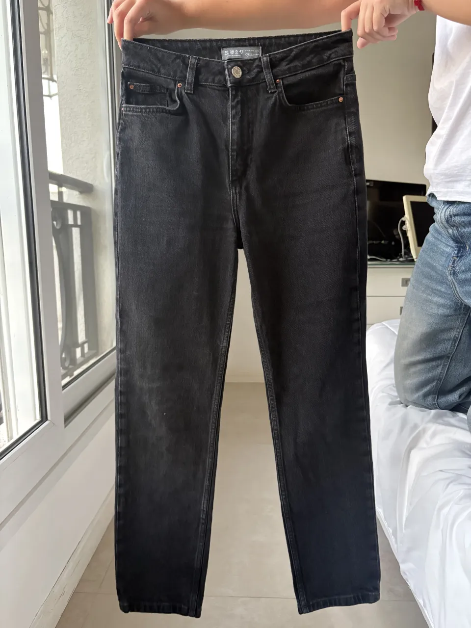 Jeans negros de tiro alto con cinco bolsillos. Cierre con botón y detalle de remaches metálicos.