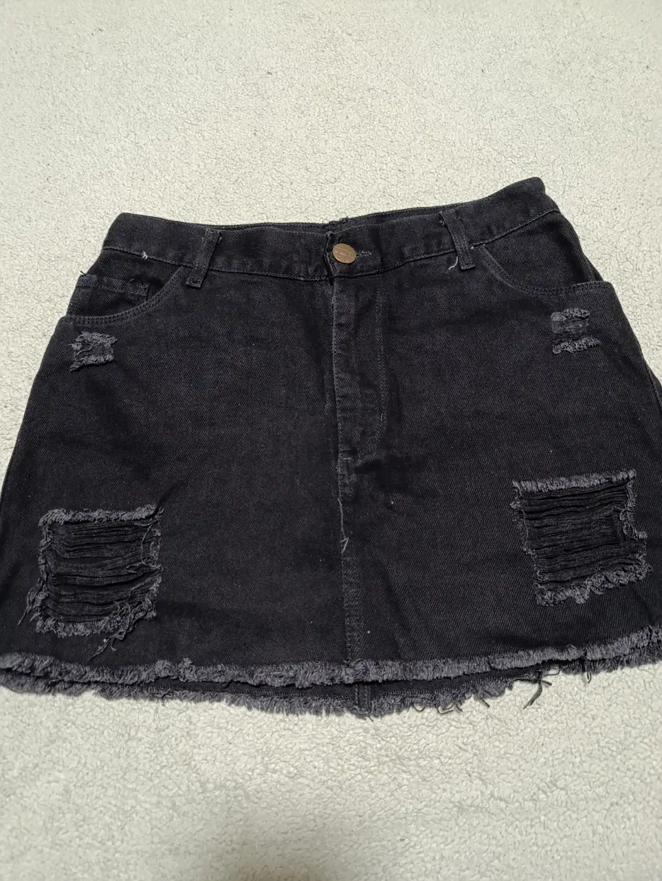 Minifalda de jean negra con detalles rotos y flecos en el borde. Ideal para un look casual y moderno.