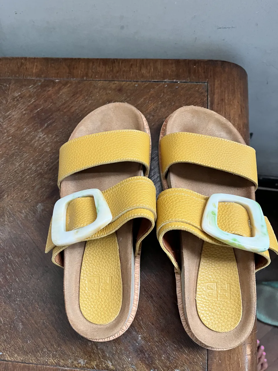 Sandalias amarillas con dos tiras y hebillas cuadradas blancas con detalles verdes. Suela de goma.