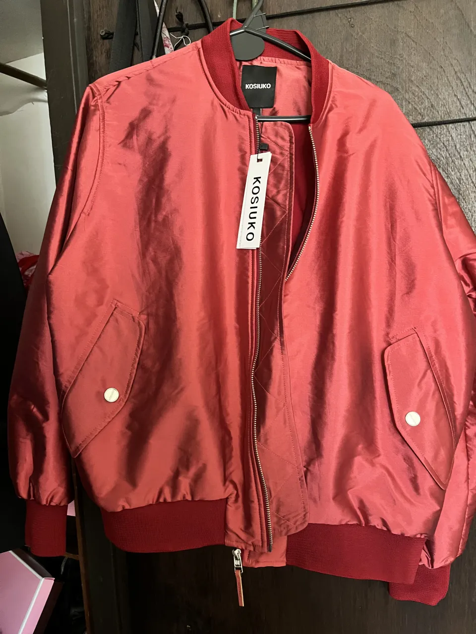 Campera bomber fuccia a con cuello, puños y cintura de ribb. Tiene bolsillos laterales con botones a presión y un bolsillo con cierre en la manga izquierda. Cierre principal metálico.