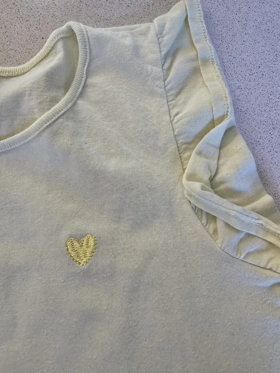 Remera súper tierna de algodón color amarillo pastel con un bordado de corazón dorado en el frente. Tiene detalles de volados en las mangas cortas. Ideal para el día a día o para un look casual y dulce.