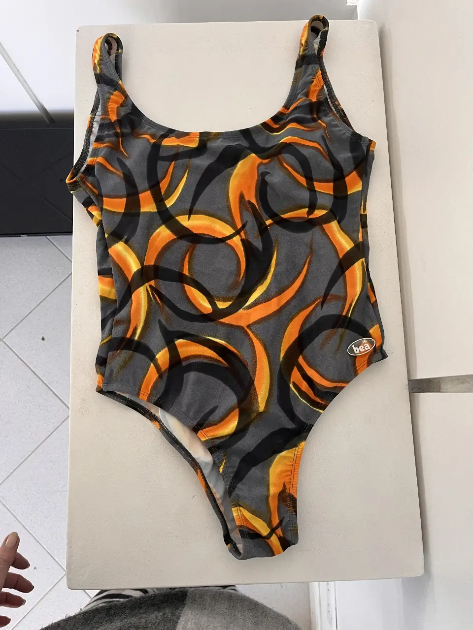 Traje de baño enterizo de mujer, con estampado abstracto en tonos grises, negros y naranjas. Ideal para la playa o la pileta.