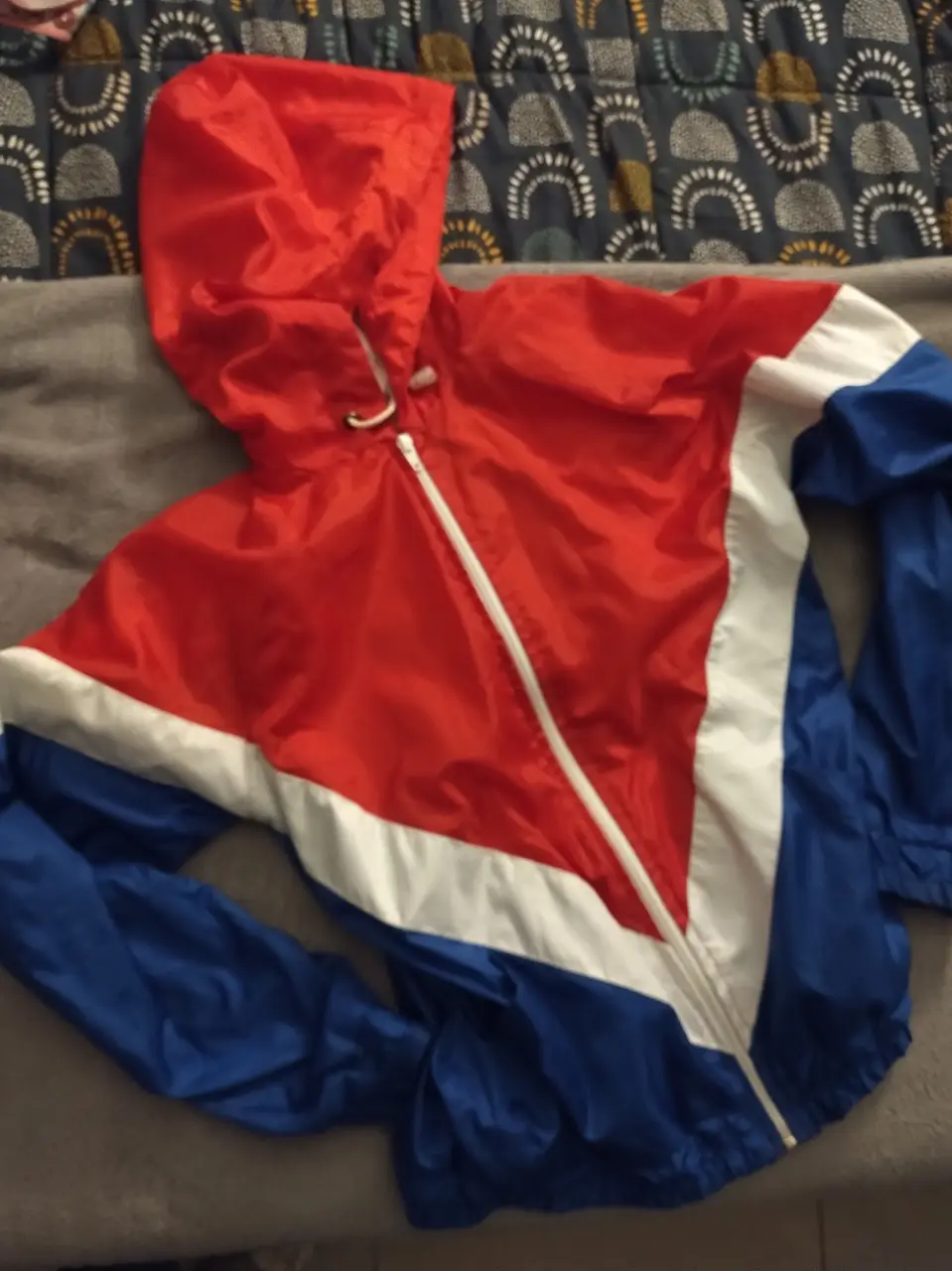 Campera rompevientos tricolor con capucha. Diseño deportivo con rojo, blanco y azul. Ideal para actividades al aire libre.
