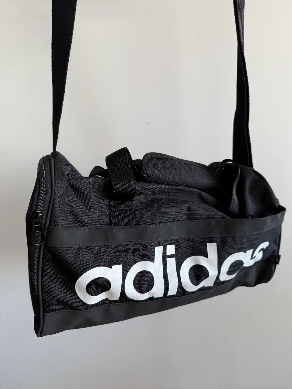 Bolso deportivo Adidas negro con logo blanco. Ideal para llevar al gimnasio o para viajes cortos. Cuenta con correa ajustable y compartimentos.
