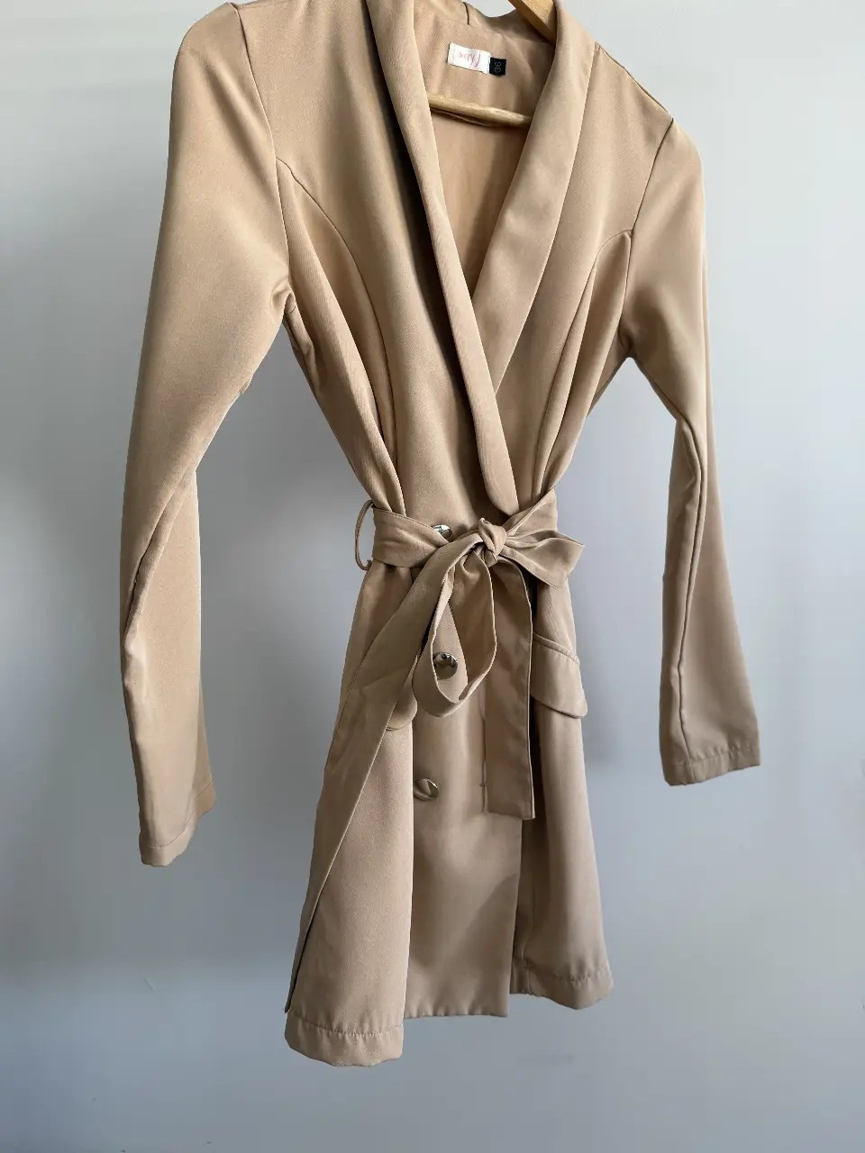 Elegante blazer vestido en color crudo, con cinturón para ajustar la cintura y botones decorativos. Ideal para un look sofisticado y versátil.