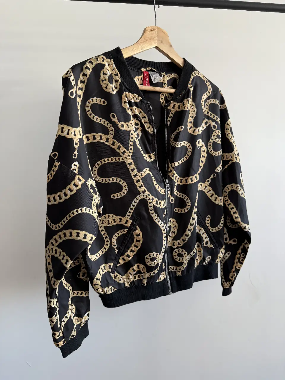 Campera bomber negra con estampado de cadenas doradas. Ideal para un look moderno y canchero. Con cierre frontal y puños elastizados. Perfecta para usar en cualquier ocasión.