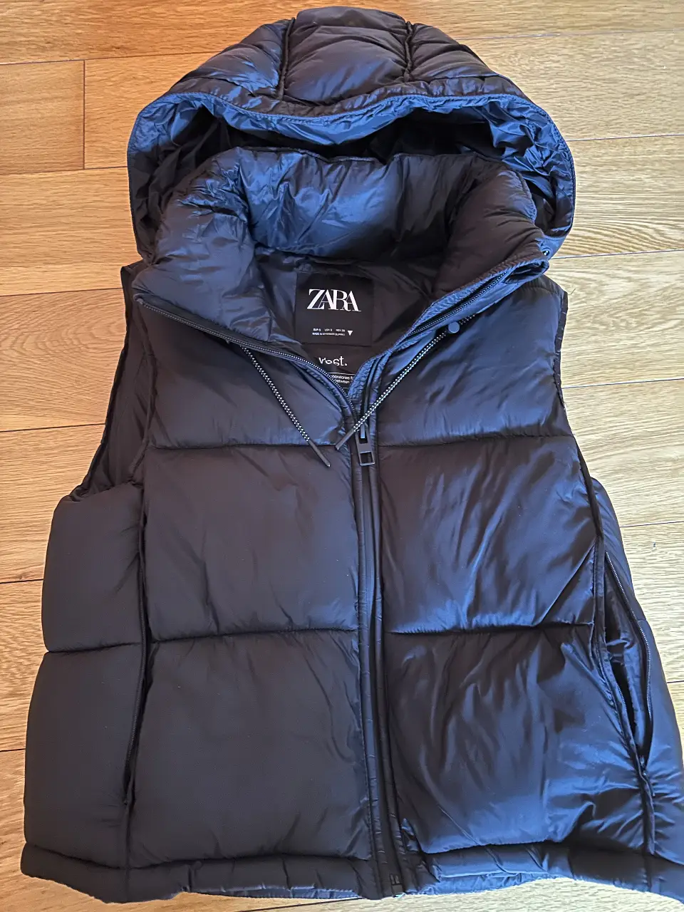 Chaleco puffer negro con capucha de la marca Zara. Ideal para el invierno, con cierre y bolsillos.