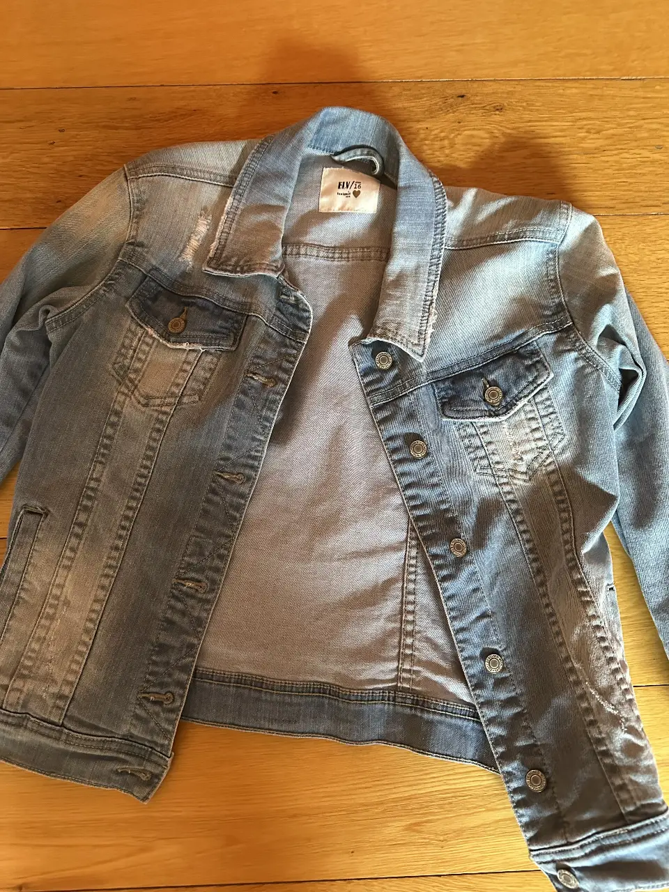 Campera de jean azul claro con detalles desgastados. Ideal para un look casual y moderno. Cuenta con dos bolsillos delanteros con botón y dos bolsillos en el pecho. Perfecta para usar en cualquier ocasión.