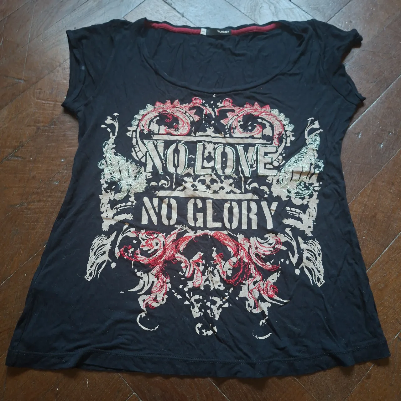 Remera negra con estampa "NO LOVE NO GLORY" en blanco, rojo y plateado. Cuello redondo y mangas cortas.