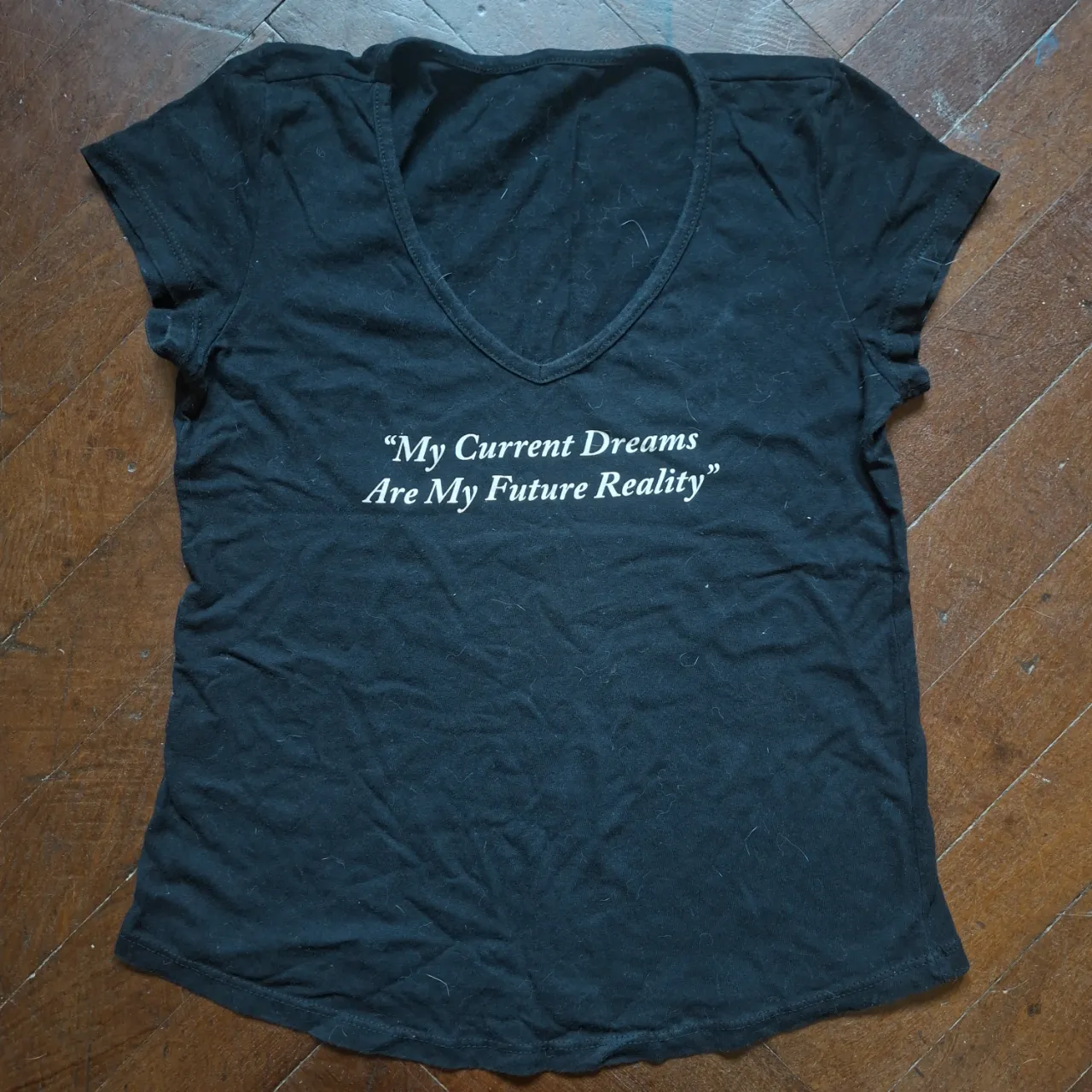 Remera negra con cuello en V y estampa "My Current Dreams Are My Future Reality" en blanco.