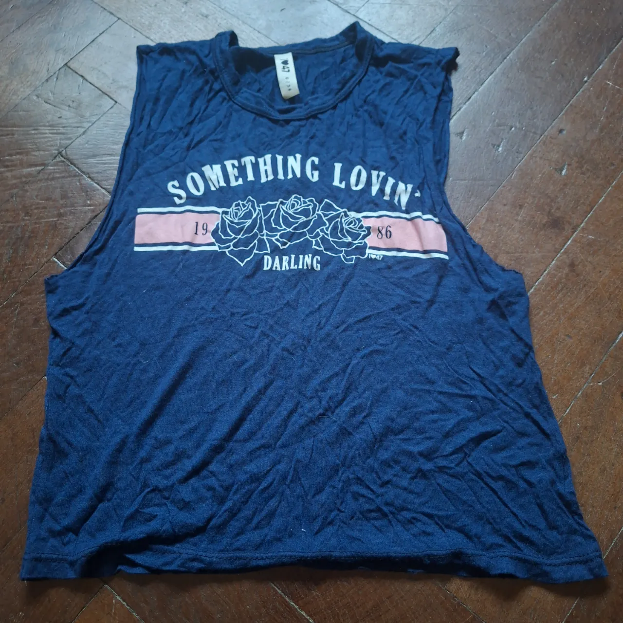 Musculosa azul marino con estampa "SOMETHING LOVIN' 19 86 DARLING" y tres rosas blancas en el frente. La estampa tiene una franja rosa pálido.