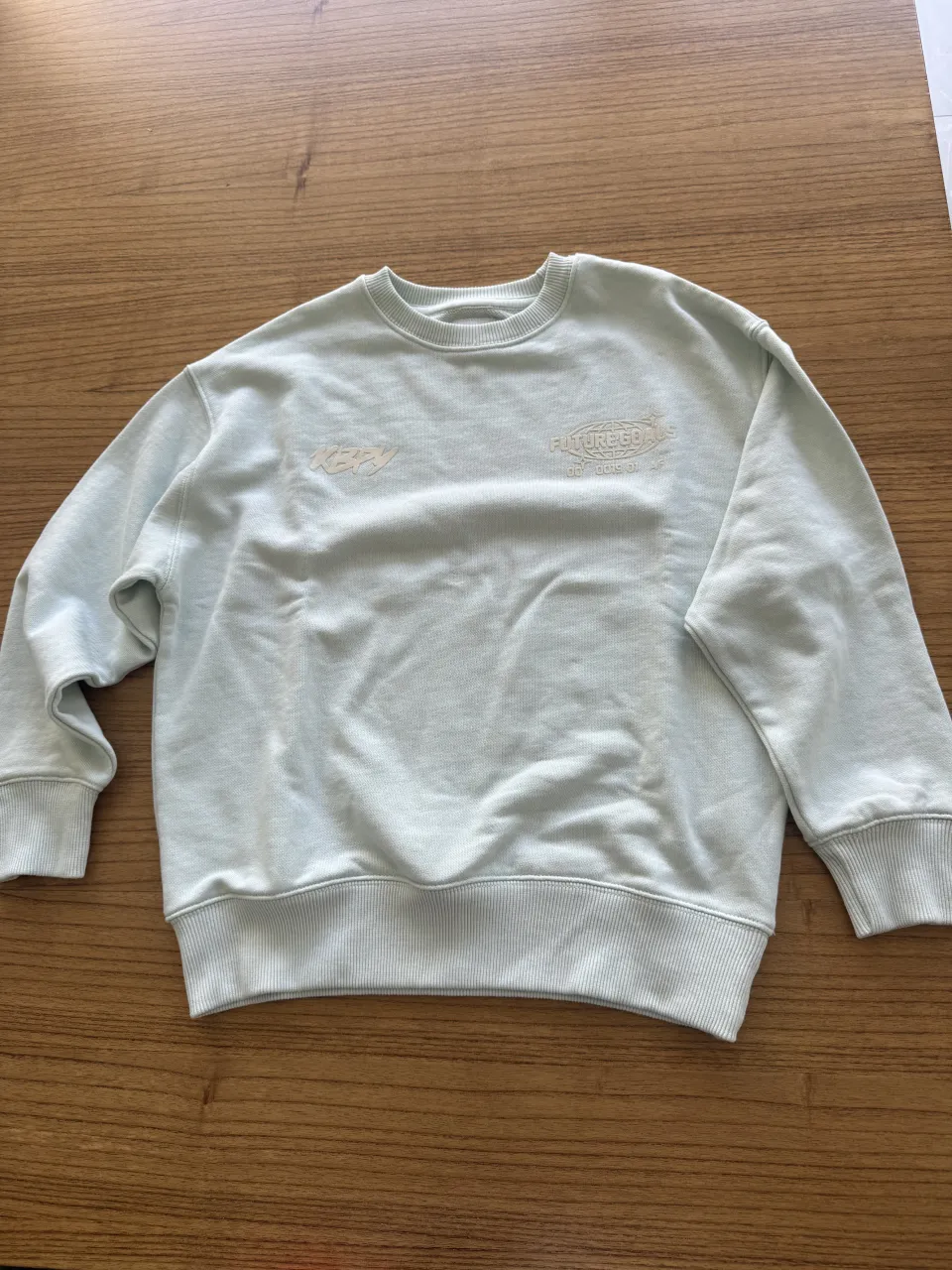 Buzo celeste con estampa "FUTUREGOALS" en el frente y "KBPRY TEAM" en la espalda. El diseño de la espalda incluye texto adicional.