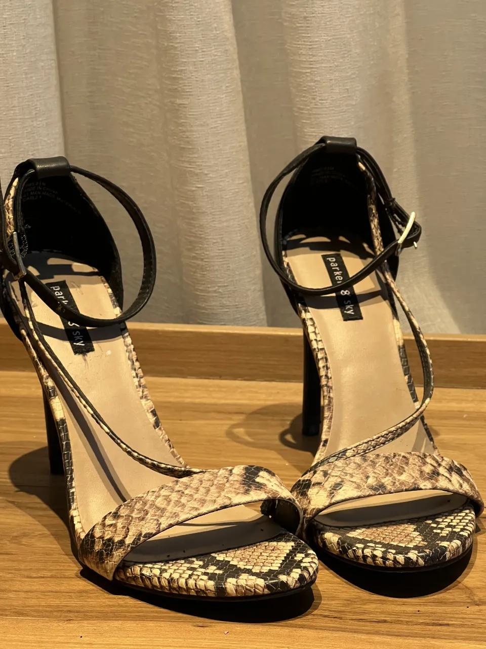 Sandalias de taco alto con tiras finas y estampa de serpiente. Cierre con hebilla en la tira del tobillo. Con una cinta que cruza y estiliza el pie.