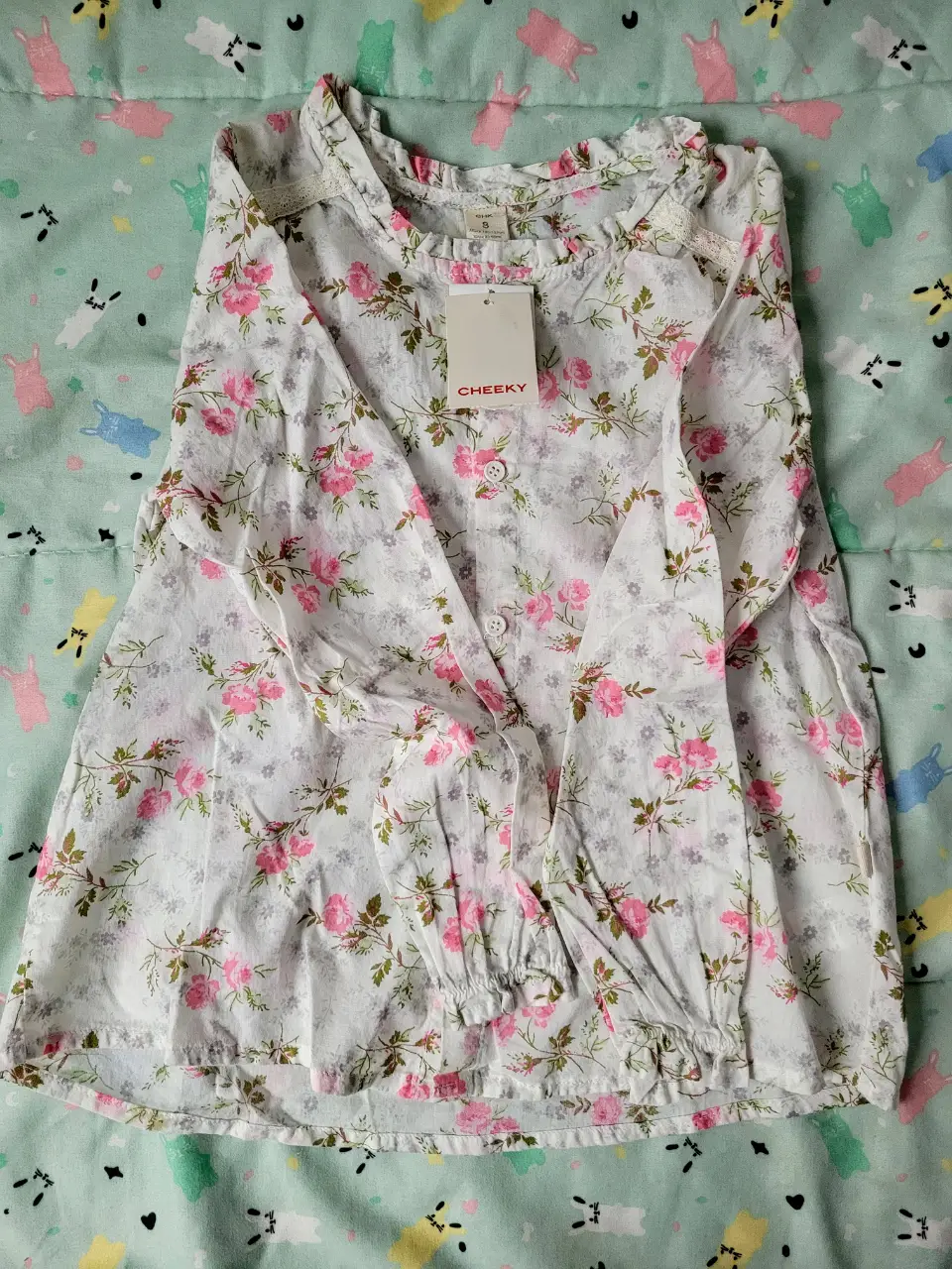 Blusa de niña con estampado floral en tonos rosa y blanco. Tiene mangas largas con puños elastizados y un cuello con volados. Ideal para un look fresco y primaveral.