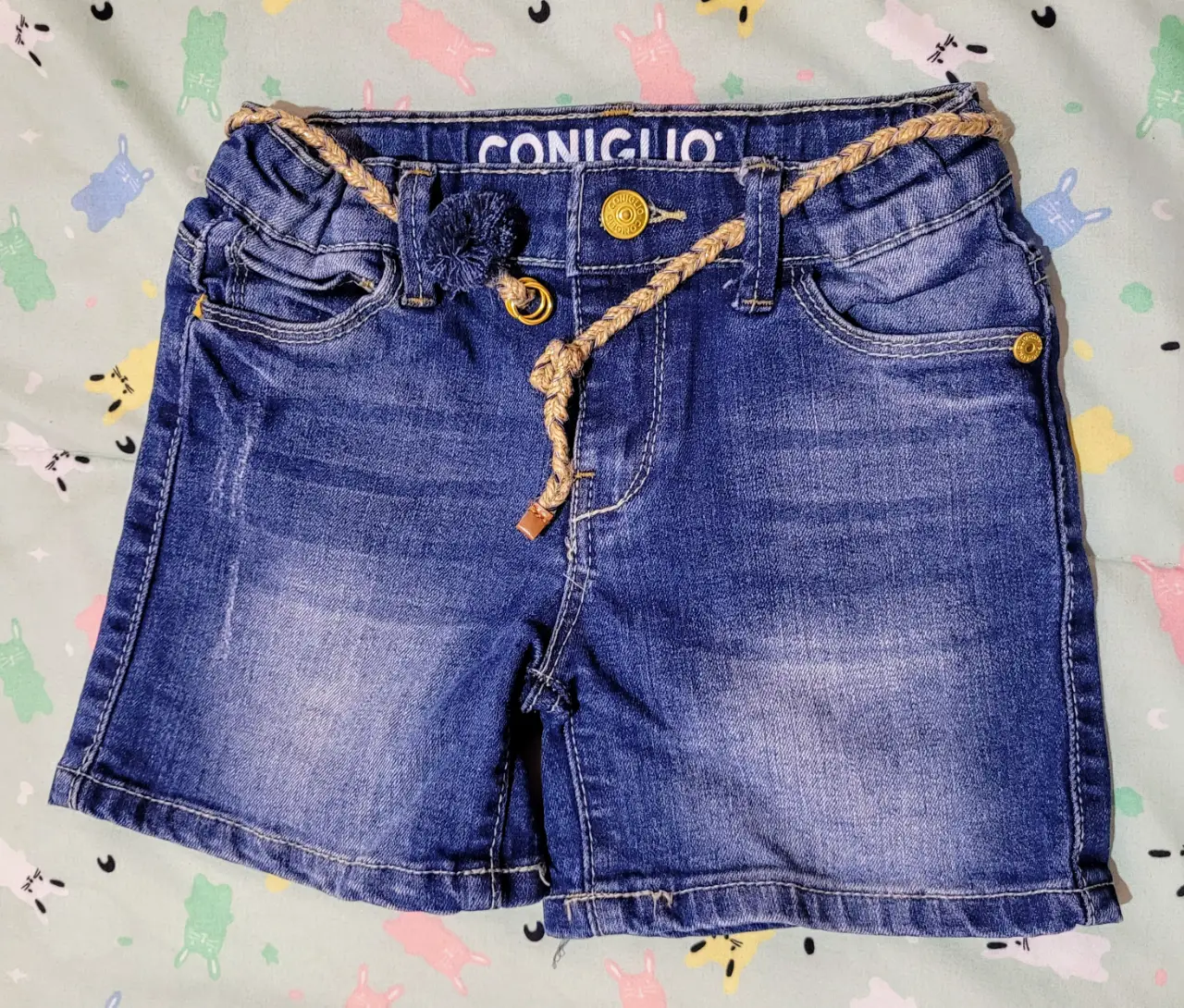 Short de jean azul para niña, con detalles de cinturón de cuerda y botones dorados. Ideal para un look casual y cómodo.