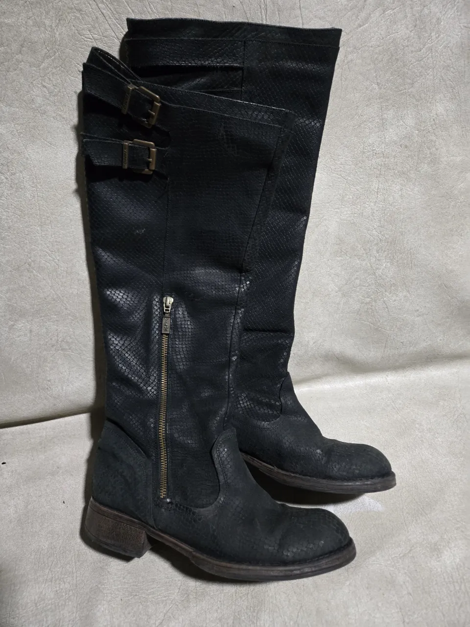 Botas de caña alta negras, con textura de serpiente y hebillas decorativas. Cierre lateral para facilitar su uso. Ideales para complementar looks urbanos y rockeros.