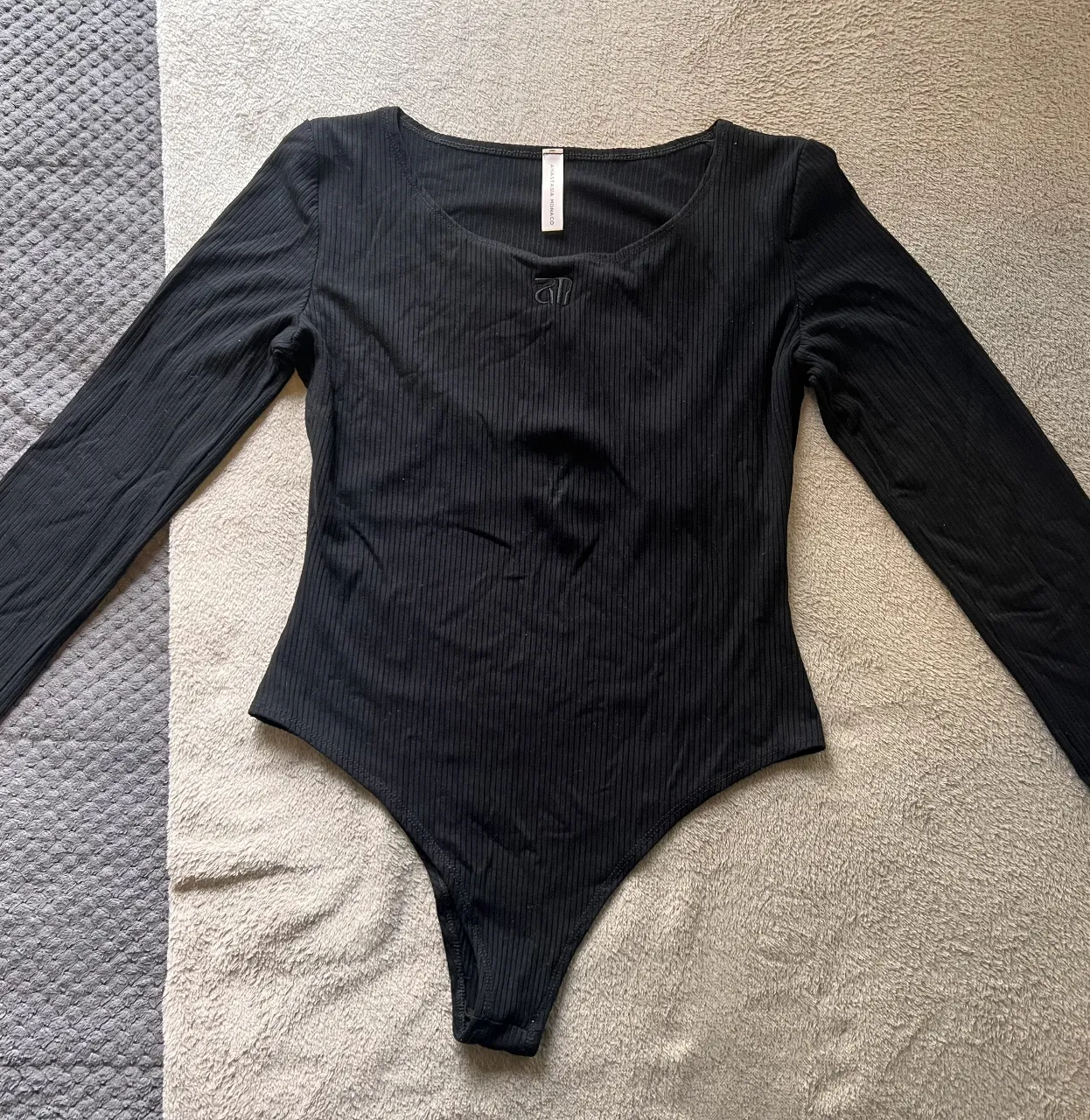 Body negro Anastasia Monaco de manga larga y corte cavado. Diseño liso con detalle de logo bordado en el frente. Ideal para un look casual y moderno.
