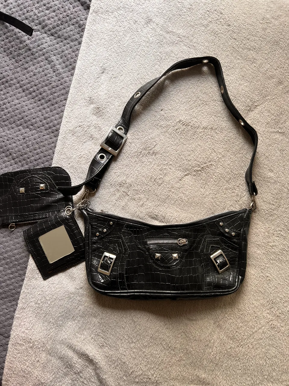 Cartera baguette negra con textura de cocodrilo, detalles metálicos plateados y un pequeño monedero a juego con espejo. Ideal para un look Y2K o rocker.