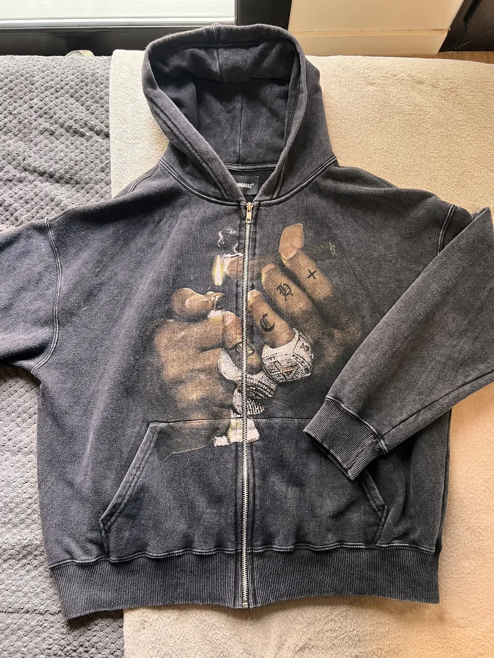 Buzo con cierre y capucha, de color gris con un estampado en la parte delantera. Ideal para un look urbano y canchero.