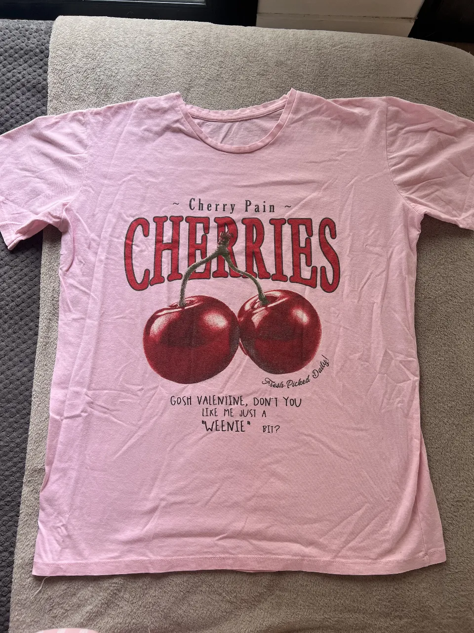 Remera de mujer de color rosa con estampado de cerezas y la frase. Estampada gastada a propósito. Muy poco uso.
